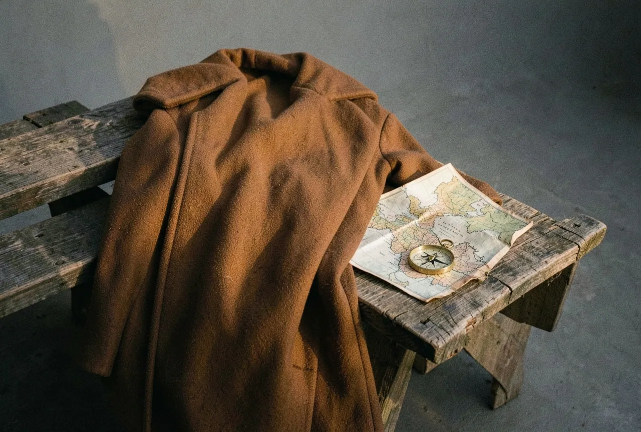 A camel coat on a wooden bench beside a paper map and a brass compass.