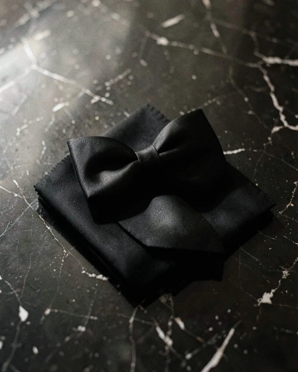 A black silk bow tie and pocket square on dark marble.