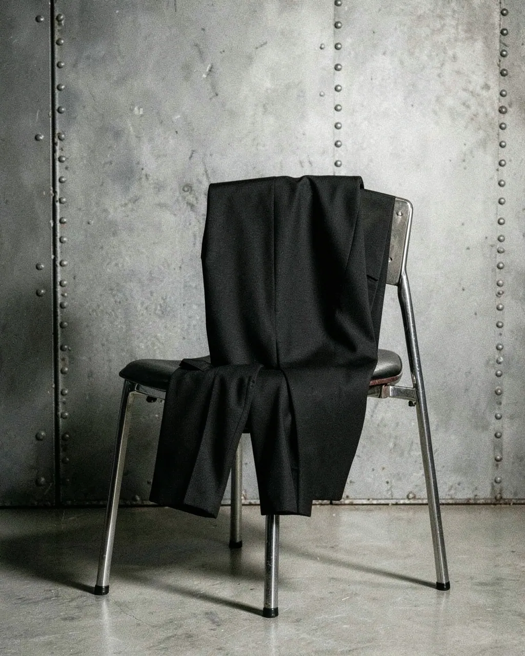 Black trousers folded over a steel chair.