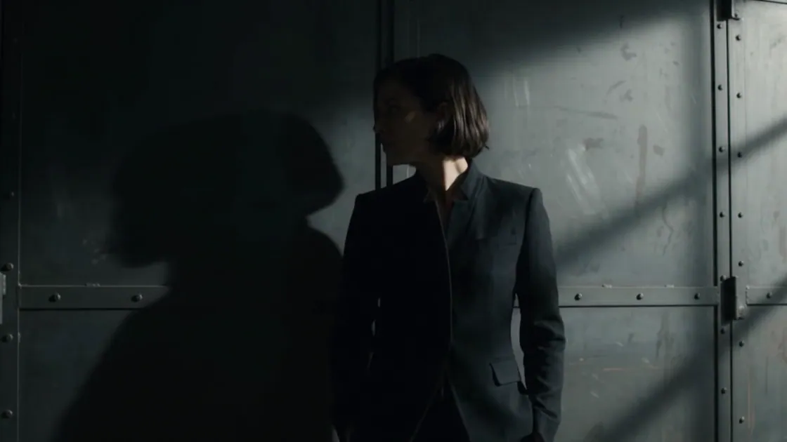 The model in black tailoring turns her head against the steel door.