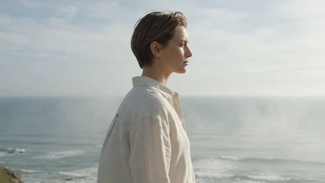 The model in cream linen turns in profile against the sea.